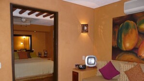 Een hotelkamer met een bed, een slaapbank, een televisie en een schilderij van fruit.