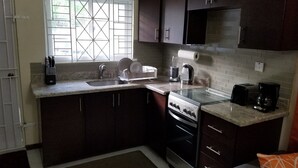 Een kleine keuken met donkere kastjes, een roestvrijstalen spoelbak, een inbouwoven en een koffiezetapparaat.