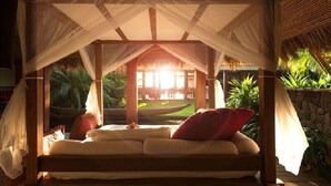 Ein Bett mit Baldachin, umgeben von üppiger Vegetation und Blick auf einen Pool.