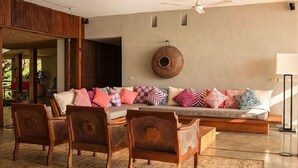 Ein modernes Wohnzimmer mit einer Sofagarnitur, gemusterten Kissen, Holzsesseln und einer runden Wanddekoration.