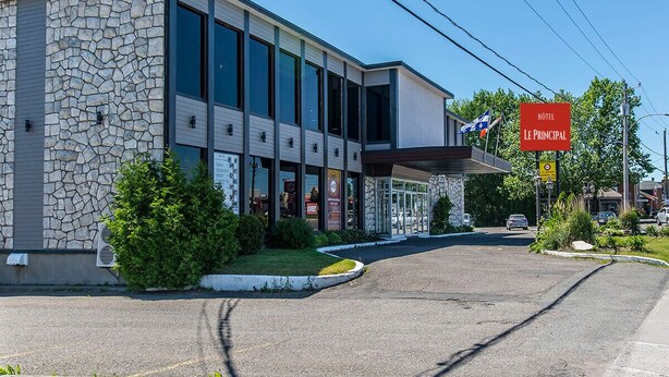 A modern hotel with a stone facade, large windows, and a prominent red sign indicating it is the main hotel. - Hotel Le Principal (Granby)