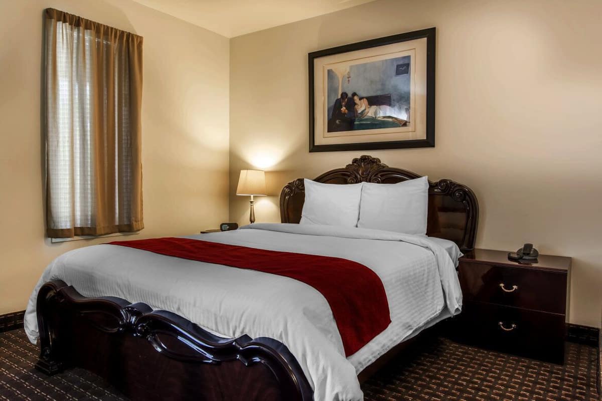 A hotel room with a large bed, a nightstand, a lamp, and a framed painting on the wall.