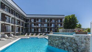 A swimming pool with lounge chairs, a stone wall, and a multi-story building with balconies. - Hotel Le Principal (Granby)
