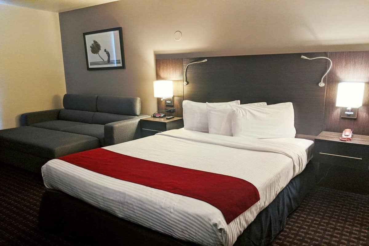 A hotel room with a large bed, a sofa, two bedside lamps, a nightstand, and a framed picture on the wall.