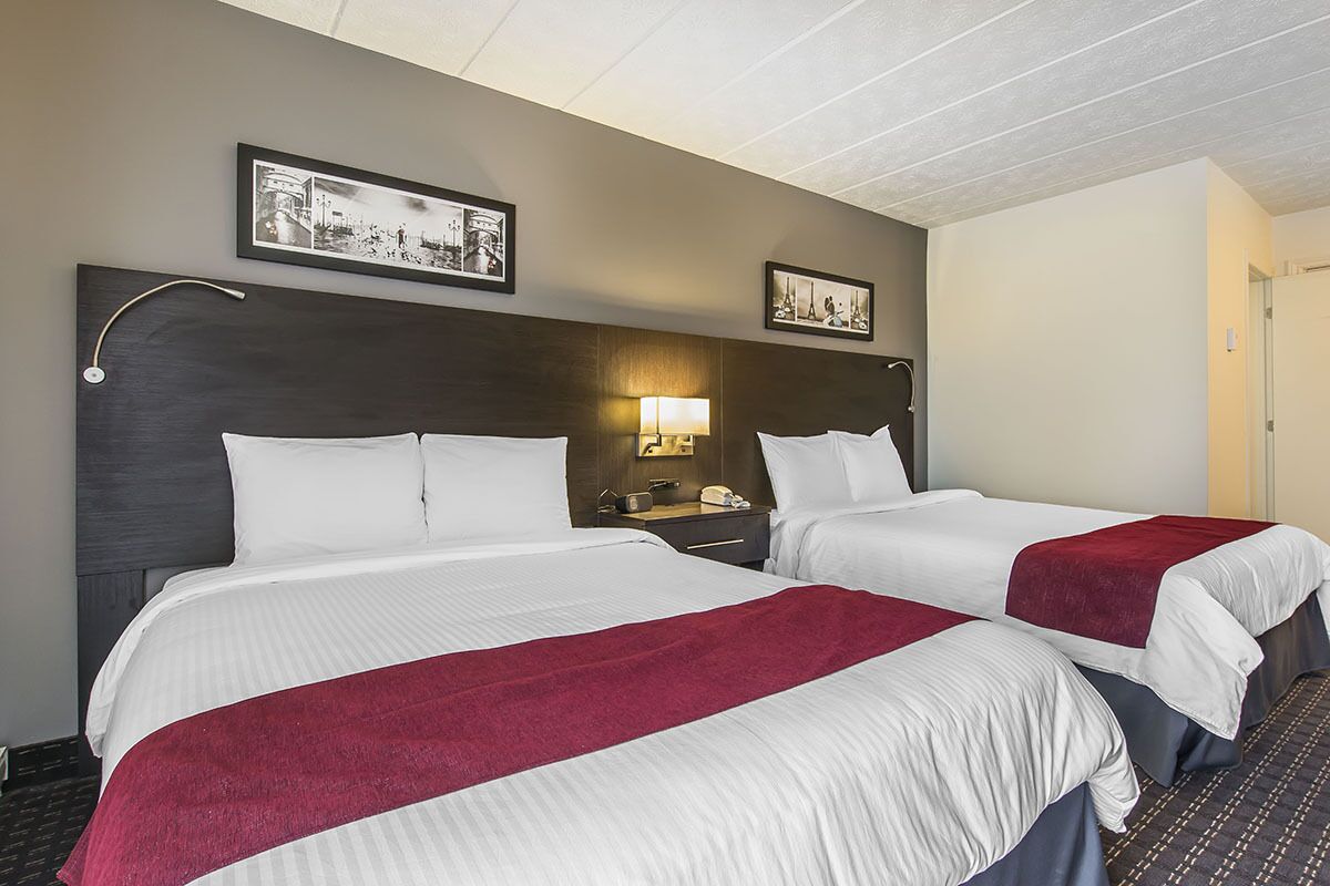 A hotel room with two beds, a nightstand with a lamp, and framed pictures on the wall.