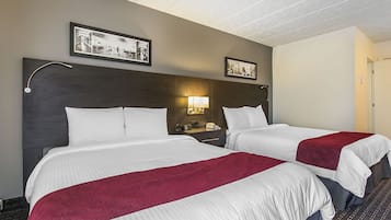 Una habitación de hotel con dos camas, una mesita de noche con lámpara y cuadros en la pared.