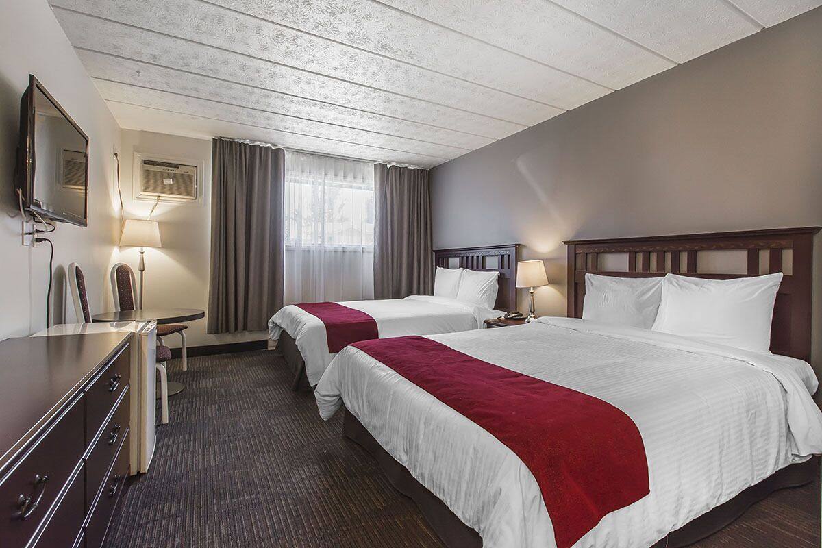 A hotel room with two beds, a desk, a chair, a TV, and a window with curtains.