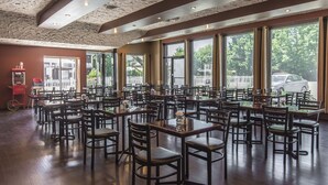 A spacious restaurant with multiple tables and chairs, large windows offering views of the outside, and a stone ceiling. - Hotel Le Principal (Granby)