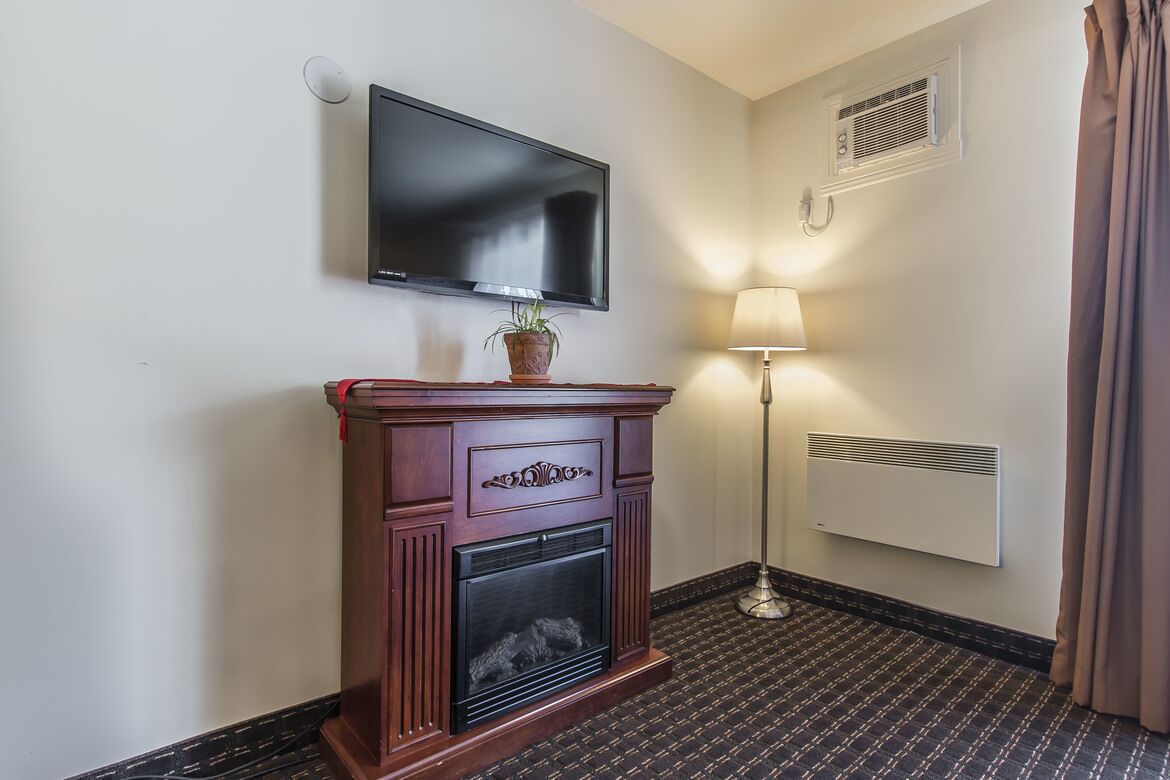 Quarto de hotel com lareira, televisão montada na parede, candeeiro de chão e radiador.