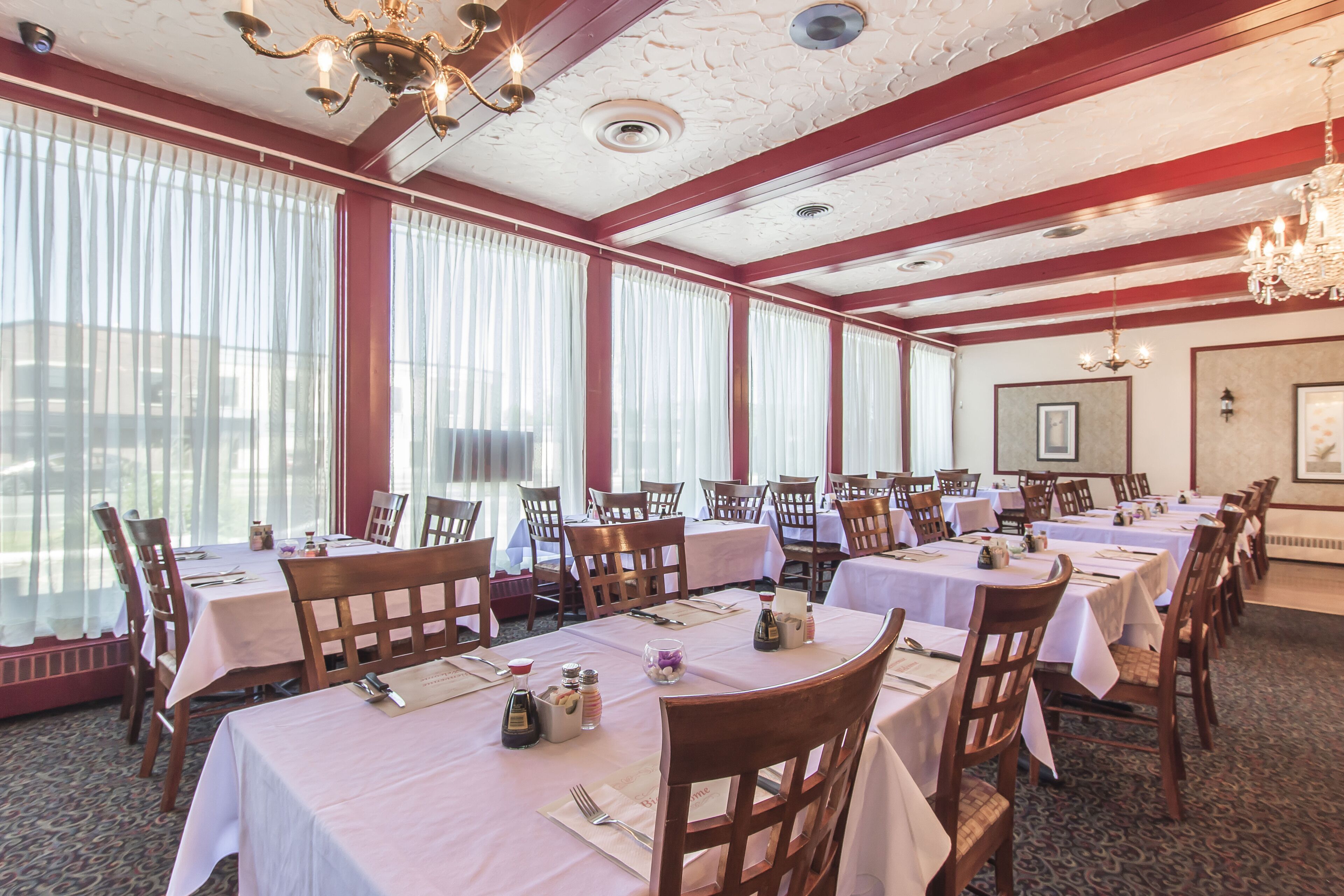 A banquet hall with multiple tables set for dining, wooden chairs, and chandeliers.