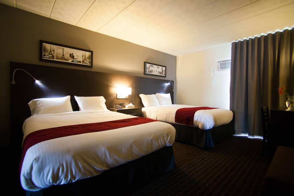 A hotel room with two beds, a nightstand, a lamp, and a picture of the Eiffel Tower on the wall.