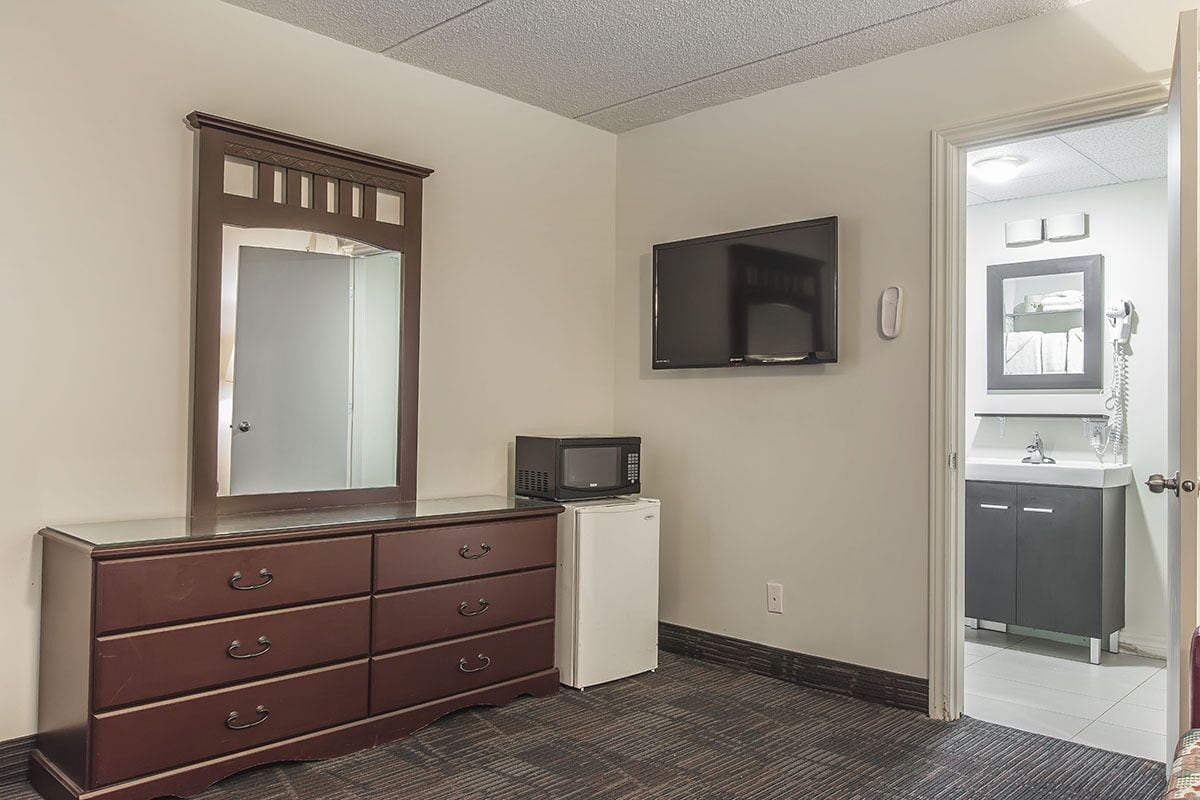 Habitación de hotel con un espejo grande, televisor de pantalla plana, microondas y refrigerador pequeño.