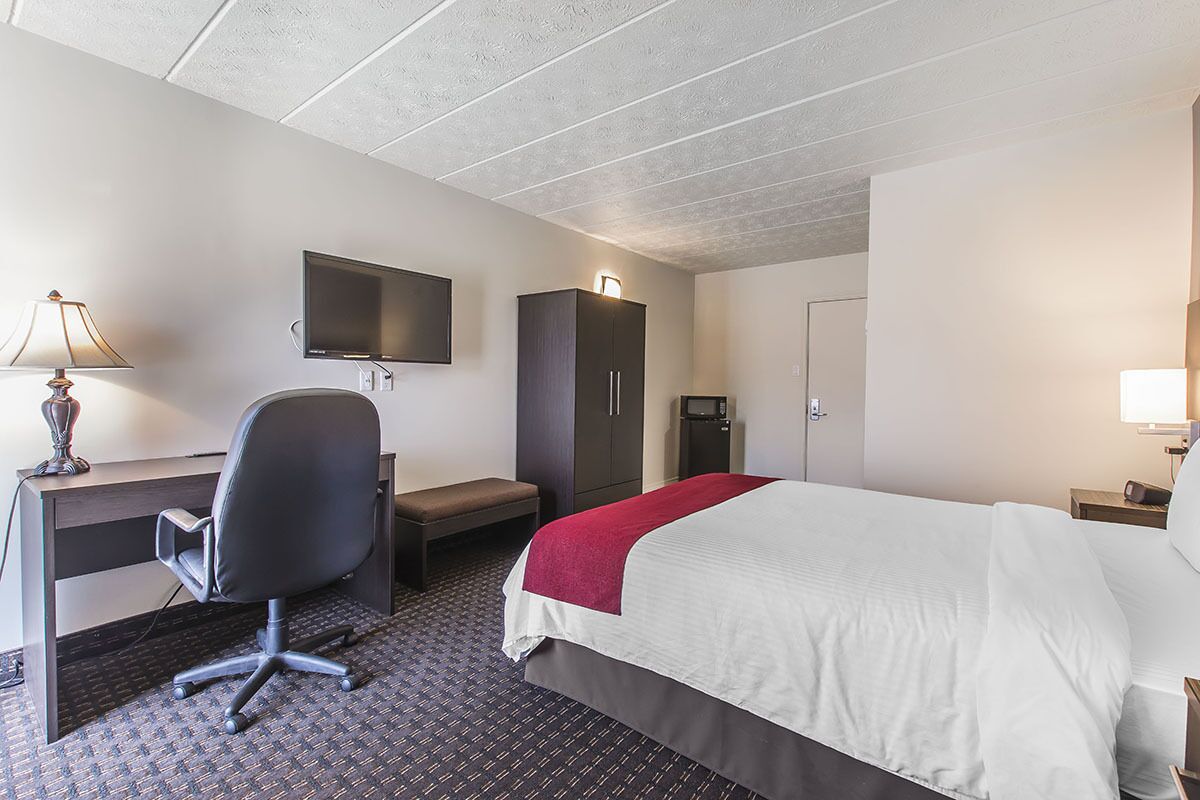 Une chambre d’hôtel comprenant un lit, un bureau, une chaise, une télévision, une armoire et une salle de bain.