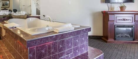 A bathroom with a large bathtub, a mirror, a television, and a fireplace.