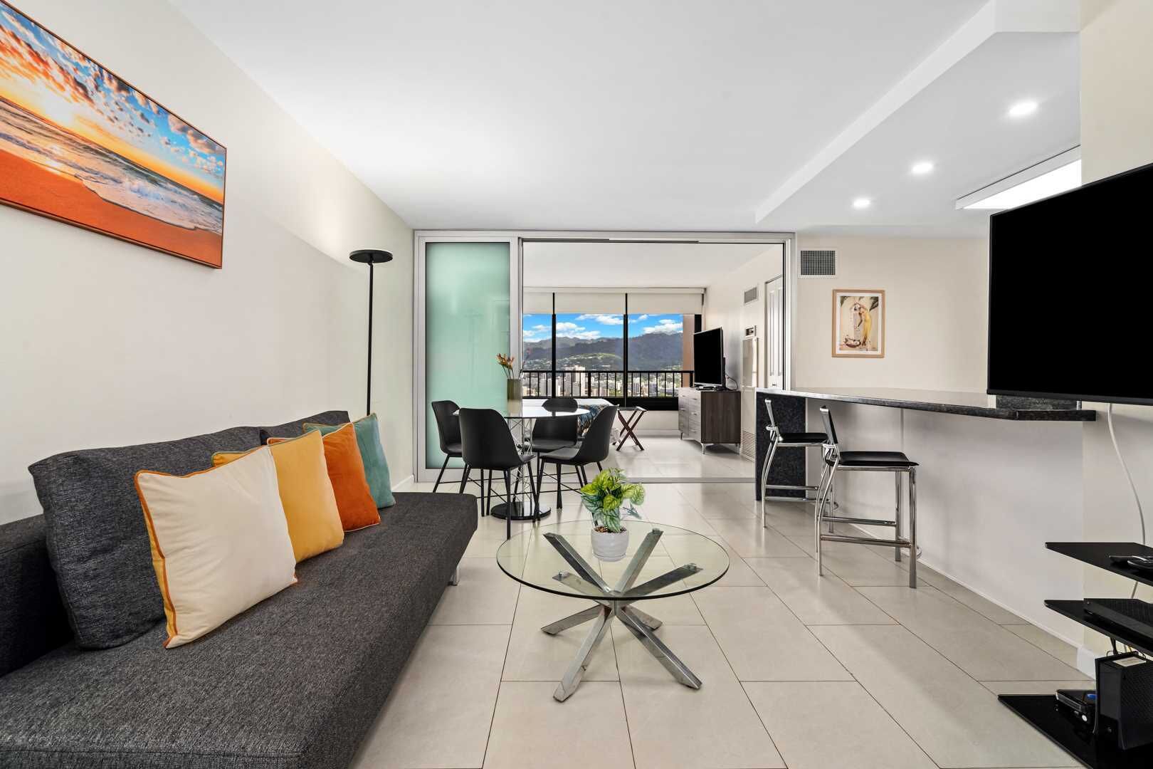 Una sala de estar moderna con un sofá gris, una mesa de centro de vidrio y una zona de comedor con sillas y una mesa.