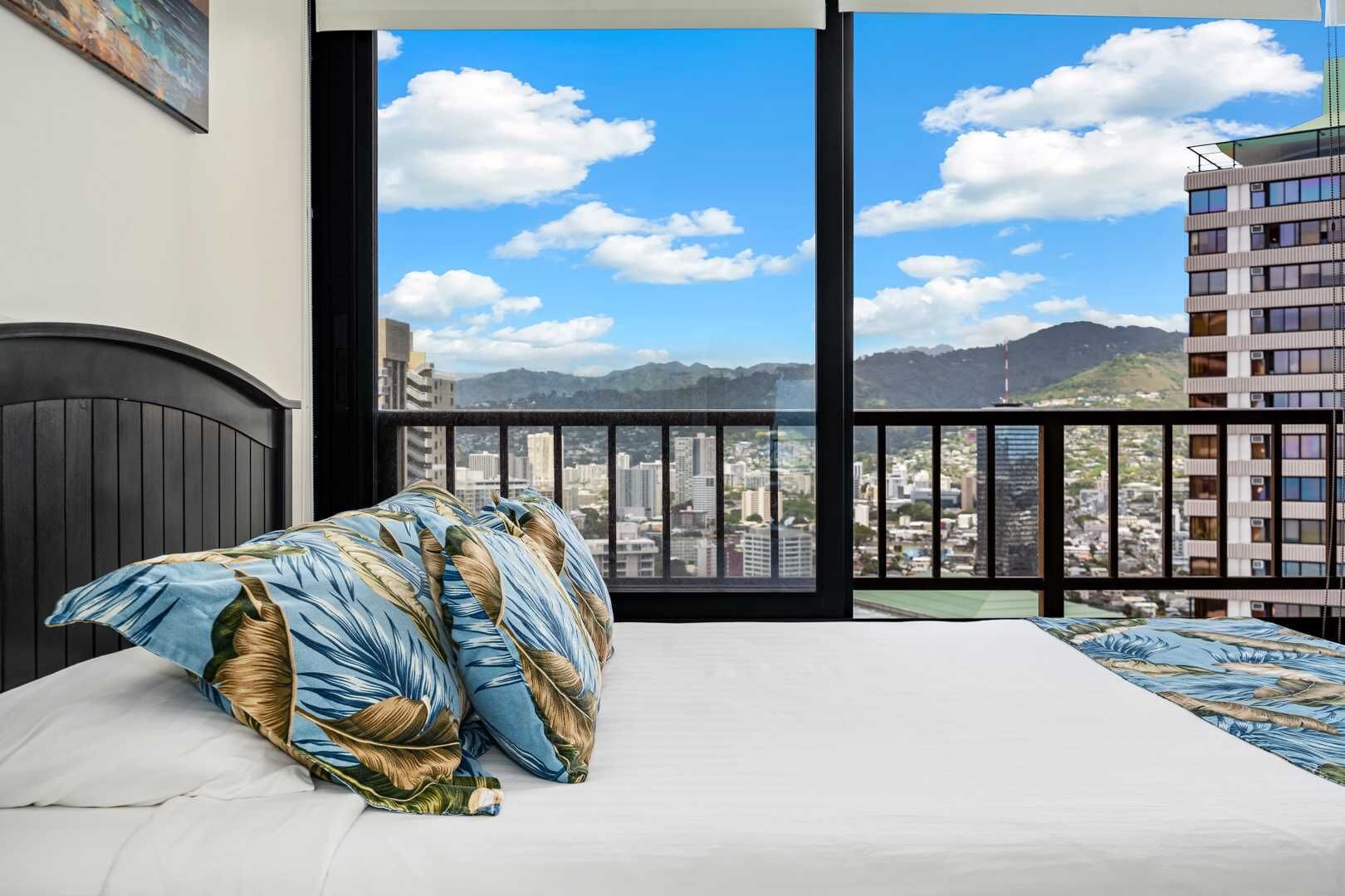 Camera da letto con un letto, vista sulla città attraverso ampie finestre e un balcone con ringhiera.