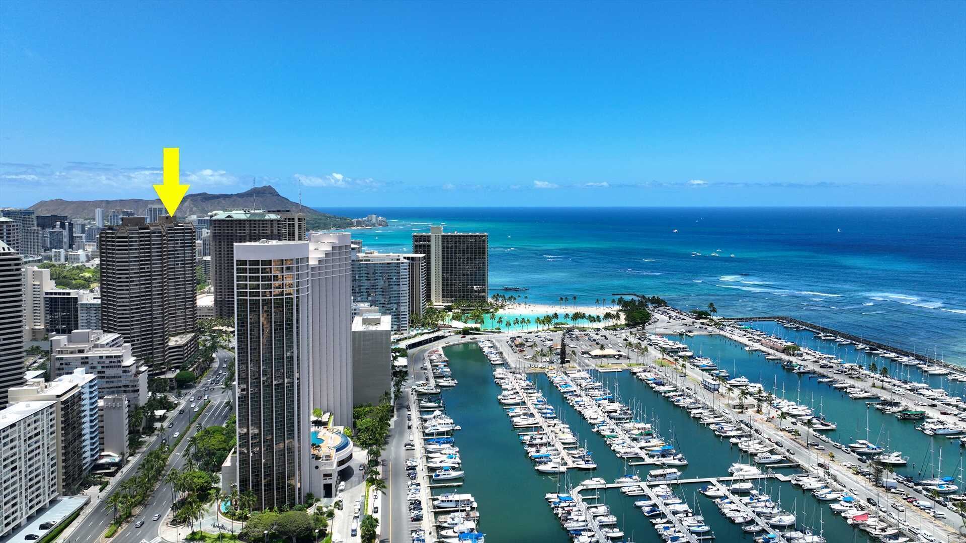 A marina with numerous boats docked, surrounded by high-rise buildings and a clear view of the ocean.