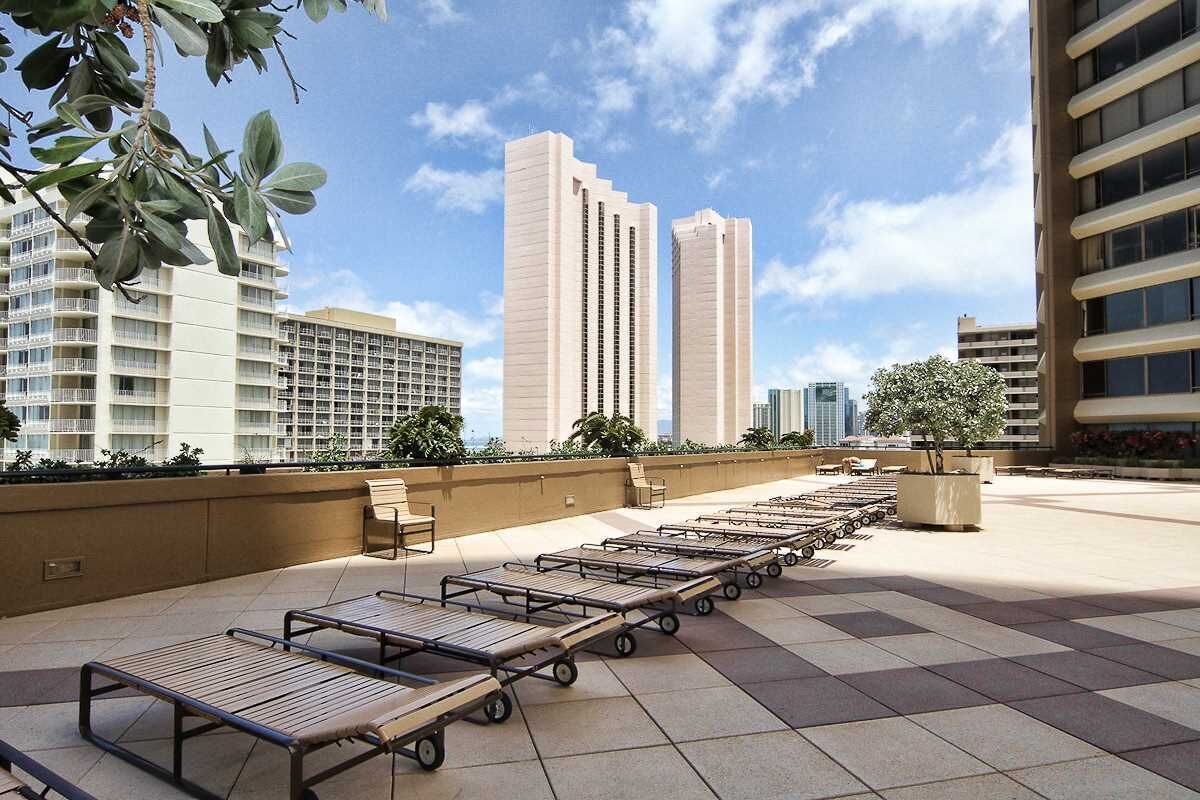 Une terrasse sur le toit, dotée de chaises longues et de transats, entourée d’immeubles de grande hauteur et offrant une vue sur un ciel dégagé.