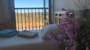 A room with a bed, a window with a view of a desert landscape, and a vase with flowers. - "Apartamento Amanecer "Vista al Campo, Golf, Piscinas, Playas - Cerca del Algarve (Ayamonte)