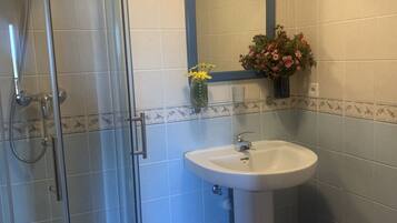 Un baño con ducha de vidrio, lavamanos pedestal y espejo sobre el lavamanos.