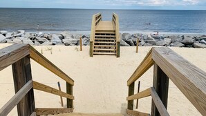 Un muelle de madera bordeando la playa, flanqueado por grandes rocas y un cielo despejado.