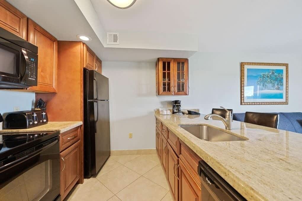 A kitchen with wooden cabinets, a microwave, a refrigerator, a sink, and a painting on the wall.