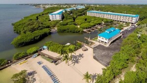 An aerial view of a resort with a large building, a beach area with sun loungers, and a water body.