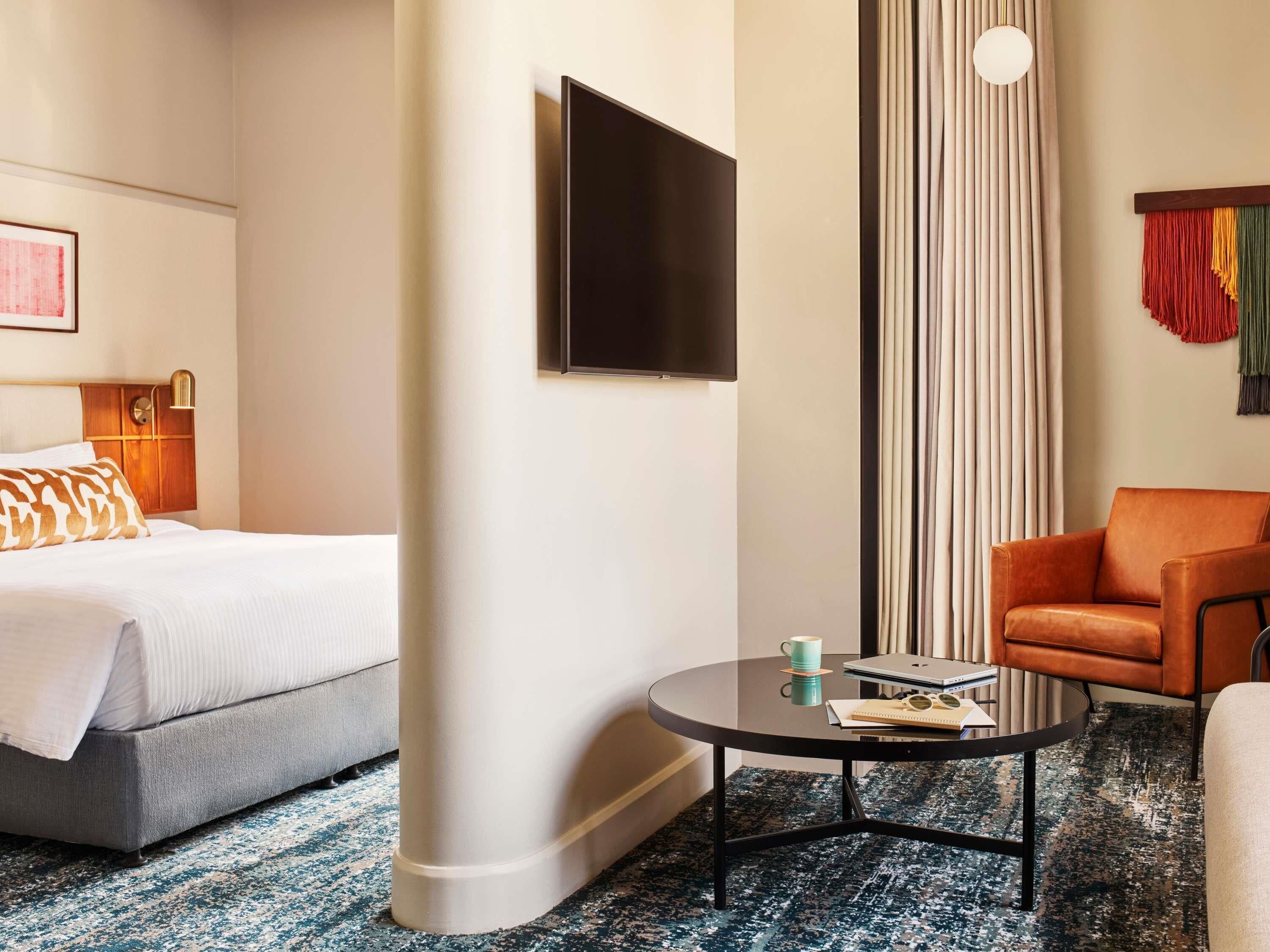 A hotel room with a bed, a round coffee table, a chair, a TV, and a window with curtains.