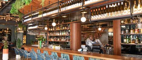A bar area with multiple seating options, a bartender, and a variety of bottles and glasses on shelves.