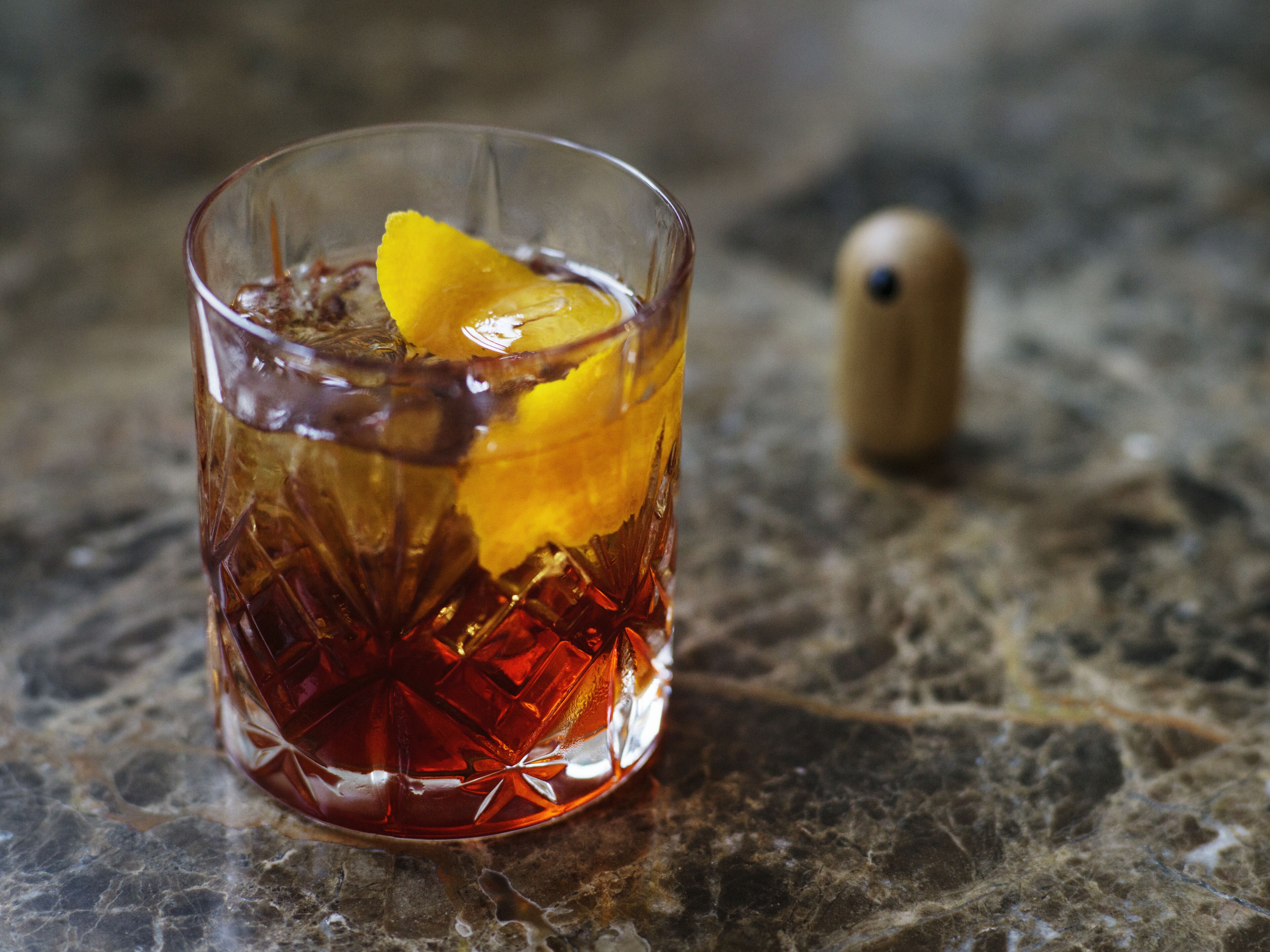 A clear glass with a yellow garnish on a marble surface.