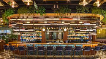 Un bar con distribución circular, múltiples estantes llenos de botellas y una barra central.