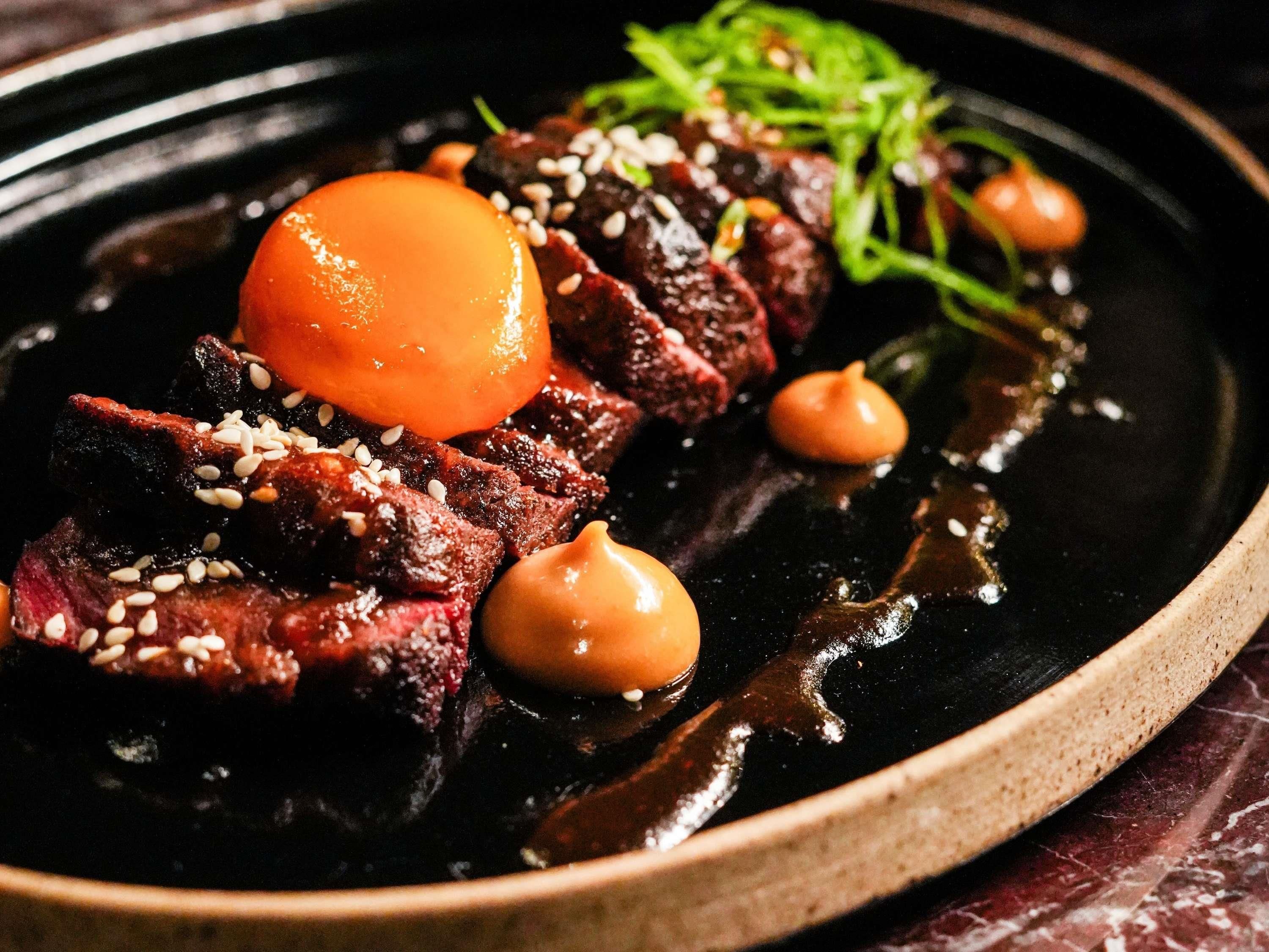 A plate of food with sliced meat, a round orange item, and a dark sauce.