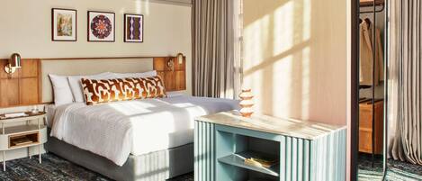 A hotel room with a bed, bedside tables, a nightstand, a console table with books, a mirror, and a window with curtains.