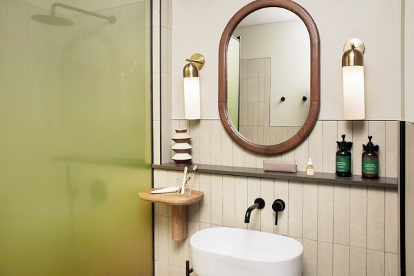 Un baño moderno con un espejo ovalado grande, un lavamanos blanco y dos luces fijadas a la pared.