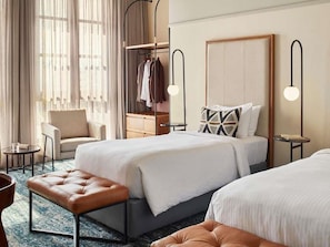 A hotel room with two beds, a seating area, a wardrobe, and a desk.