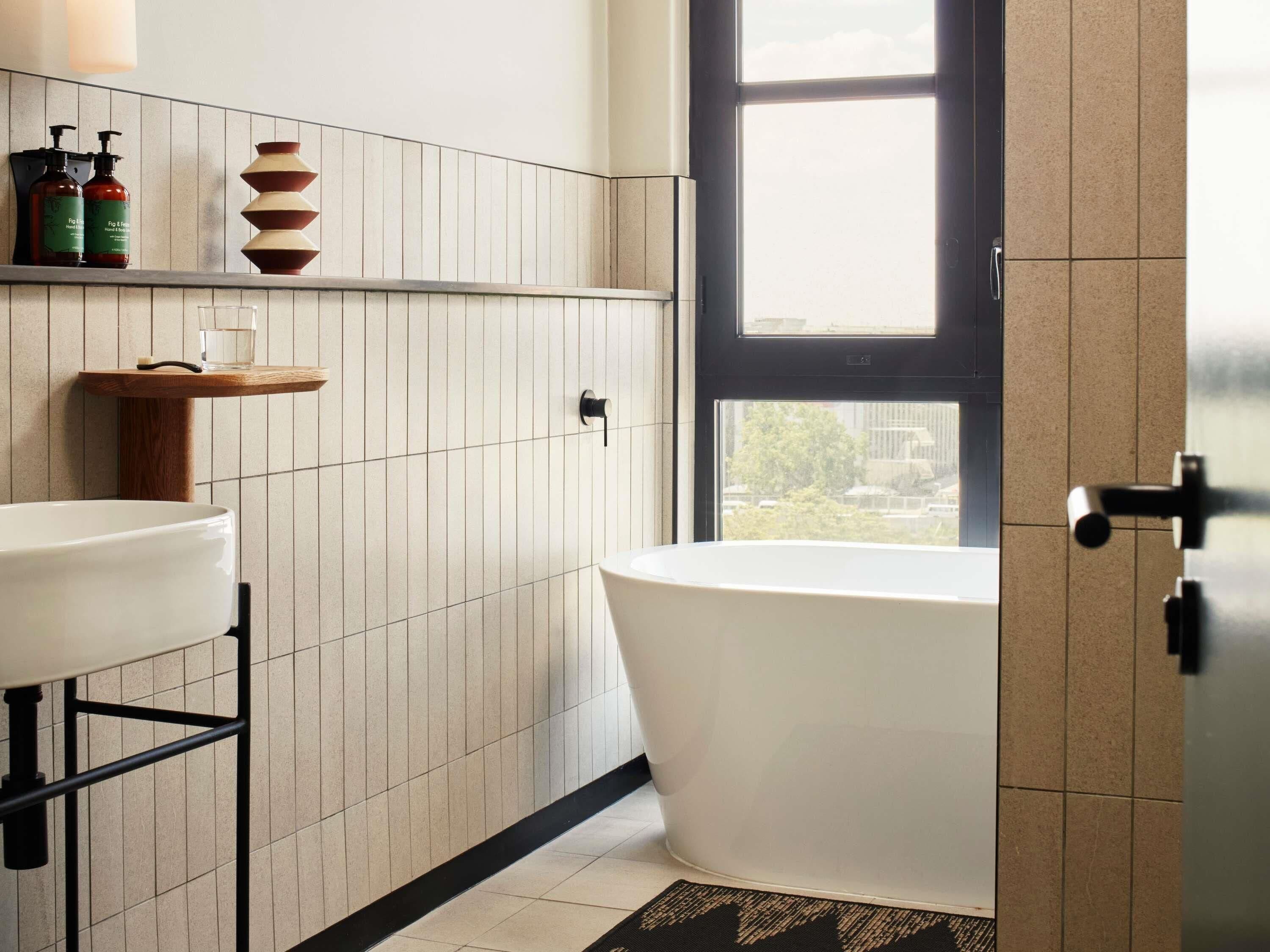 Een moderne badkamer met een vrijstaand bad, een witte wastafel en een houten plank met toiletartikelen.
