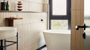A modern bathroom with a freestanding bathtub, a white sink, and a wooden shelf with toiletries.