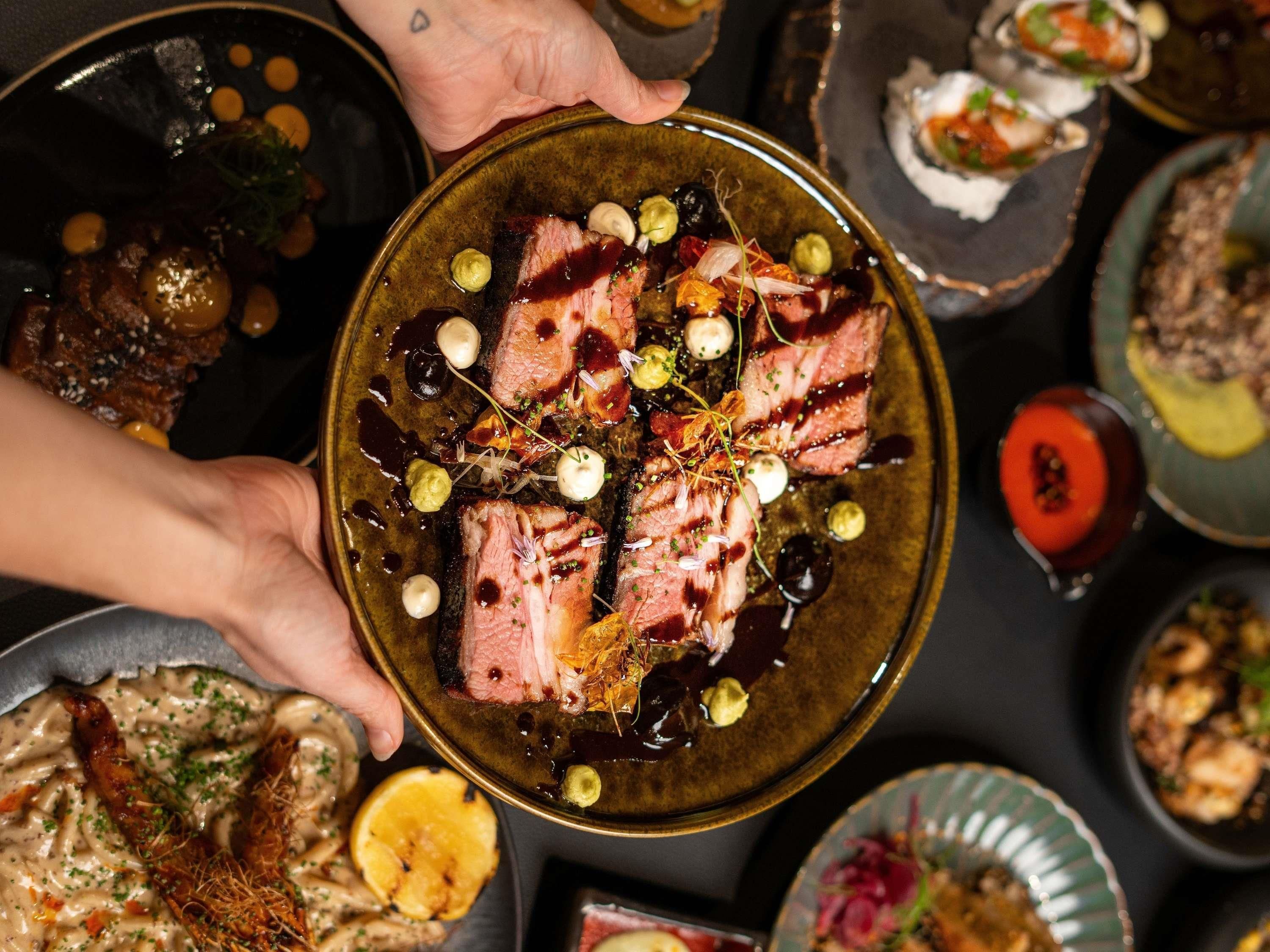 A person holding a plate with sliced meat garnished with herbs and sauce.