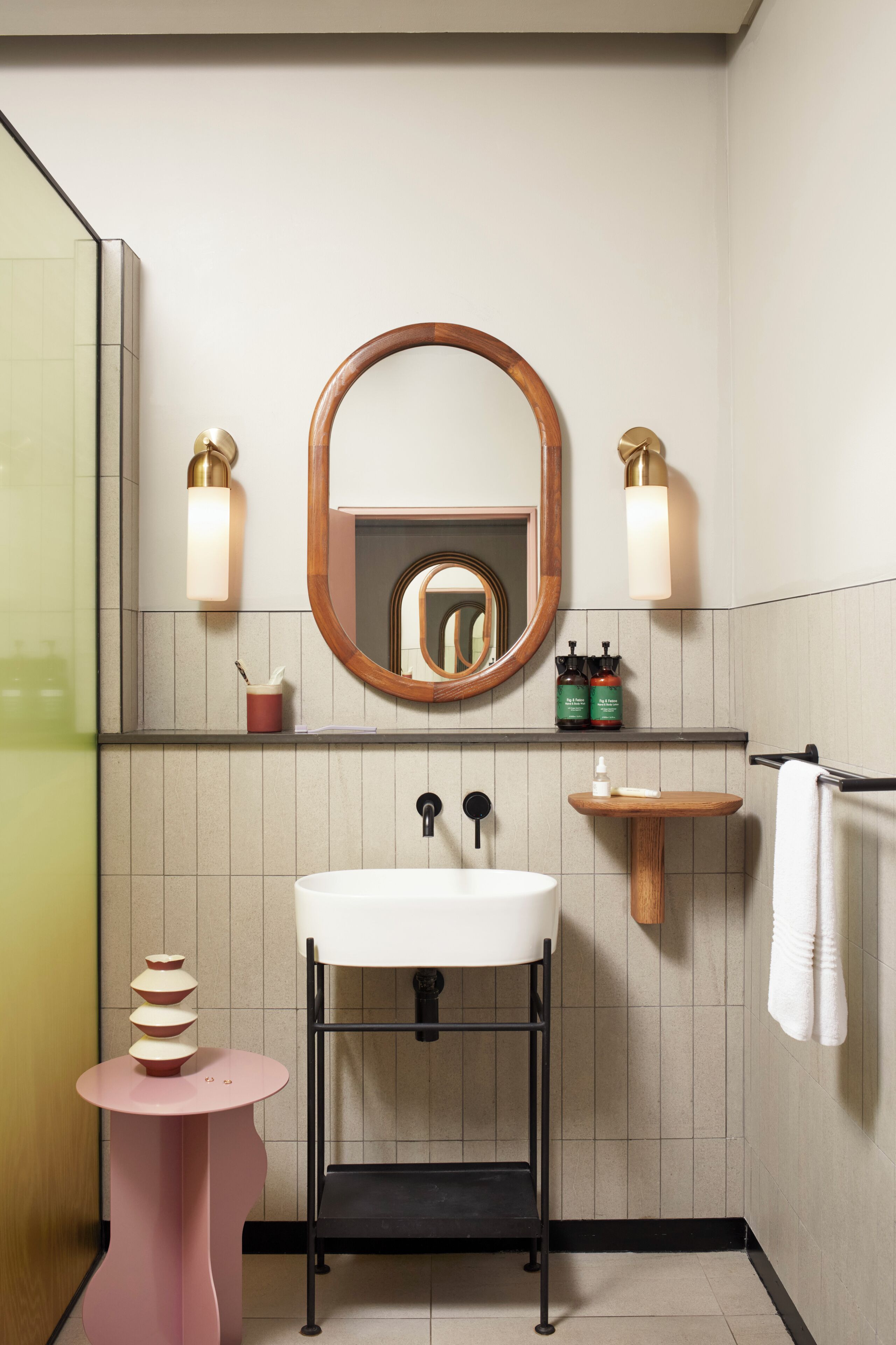 A modern bathroom with a white sink, a round mirror, and a pink side table.