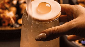 Una mano sosteniendo un vaso con pajita, conteniendo una bebida con un adorno encima.