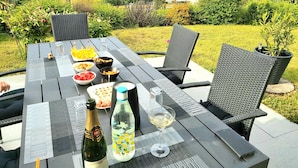 An outdoor dining table with various food items and drinks, surrounded by greenery and a scenic view of houses and mountains.