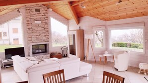 A modern living room with a stone fireplace, white furniture, and large windows offering a view of the outdoors.