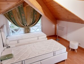 Un dormitorio con techo inclinado, una cama con colchón acolchado, una mesita de noche, un taburete pequeño y una lámpara de pie.