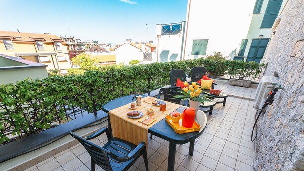 A terrace with a table set for two, chairs, a potted plant, and a water dispenser.