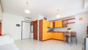A modern kitchen with yellow cabinets, a dining area with a small table and chairs, and a white sofa in a living room.