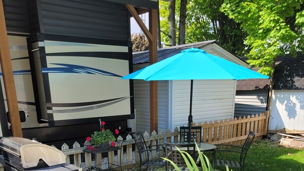 A patio area with a grill, a table with chairs, a blue umbrella, and a wooden deck. - The Big Happy Place (Fergus)