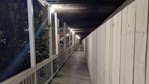 Um deck de madeira coberto com guarda-corpo, que conduz a um edifício com vários andares.