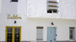 A building with a yellow door and a blue door, both with windows. The building has a sign that reads "Salitre". - Hostal Salitre (Conil de la Frontera)
