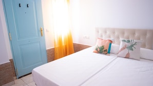 A hotel room with a light blue door, a bed with white bedding, and a tufted headboard. - Hostal Salitre (Conil de la Frontera)