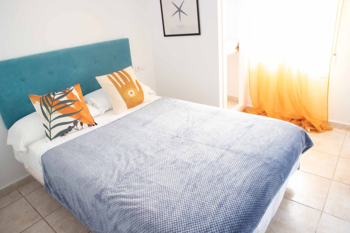 Una cama con cabecera azul, ropa de cama blanca y almohadones decorativos.